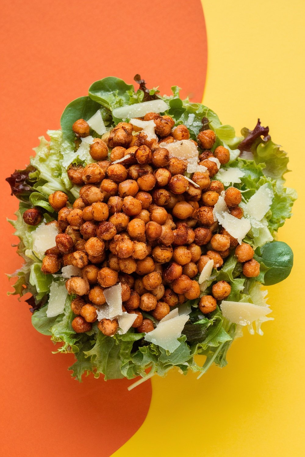 A colorful Caesar salad topped with roasted chickpeas and Parmesan cheese on a bright background.