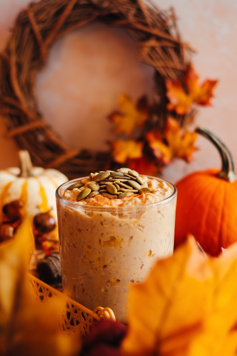 A glass of pumpkin spice overnight oats topped with pumpkin seeds, surrounded by autumn leaves and pumpkins.
